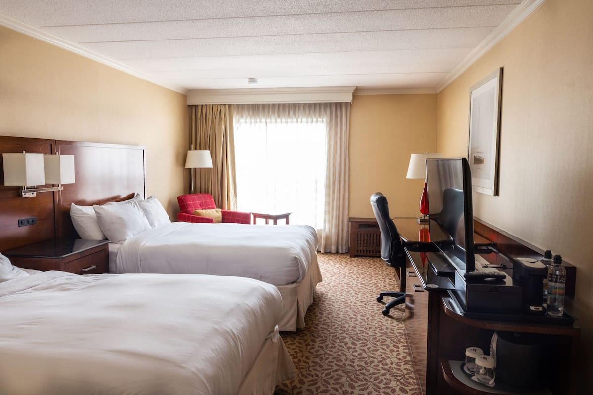 A hotel room with two beds, a desk with a computer, a chair, and a TV.