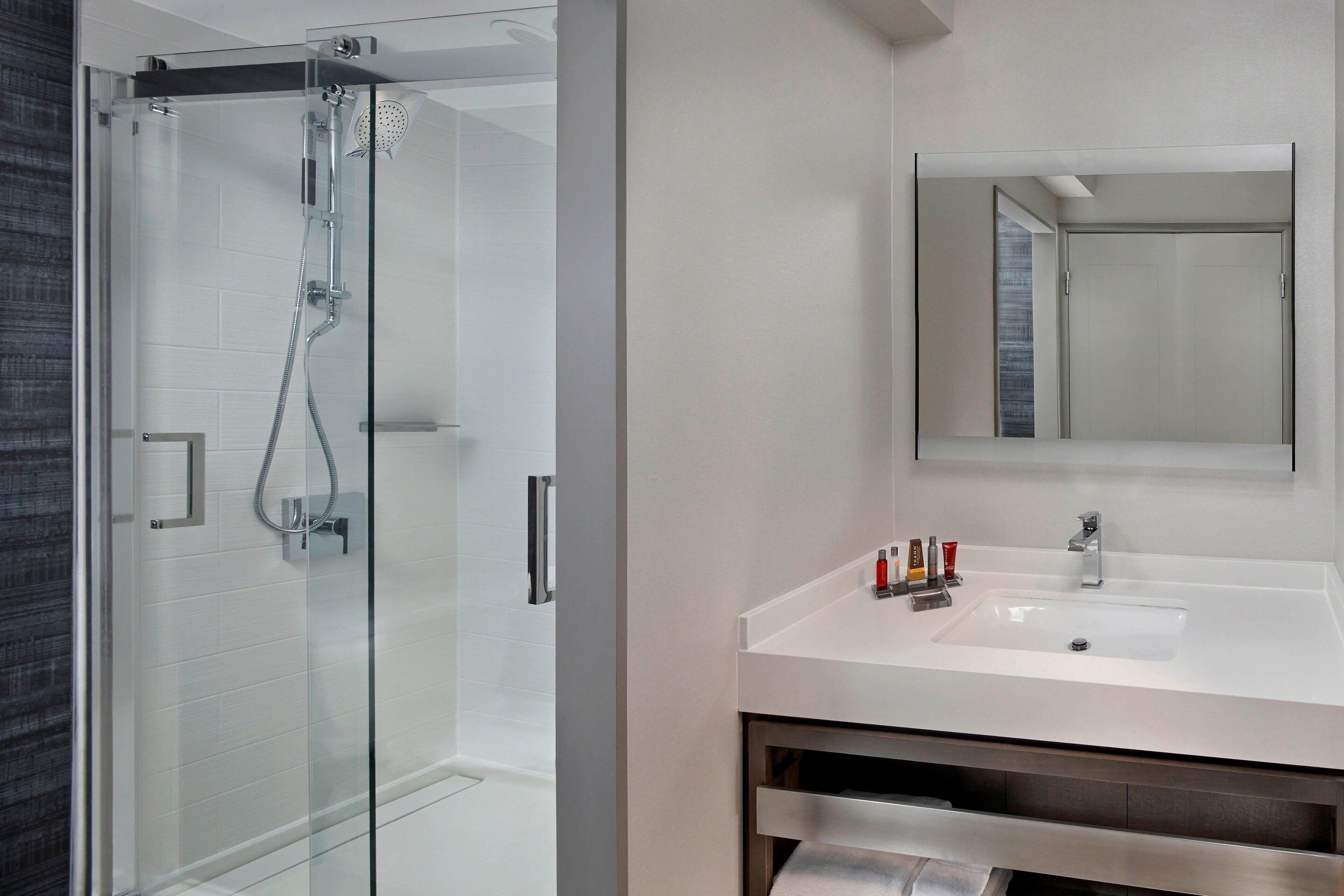 Un baño moderno con ducha envuelta en vidrio, un lavabo blanco y un espejo grande sobre el mueble.