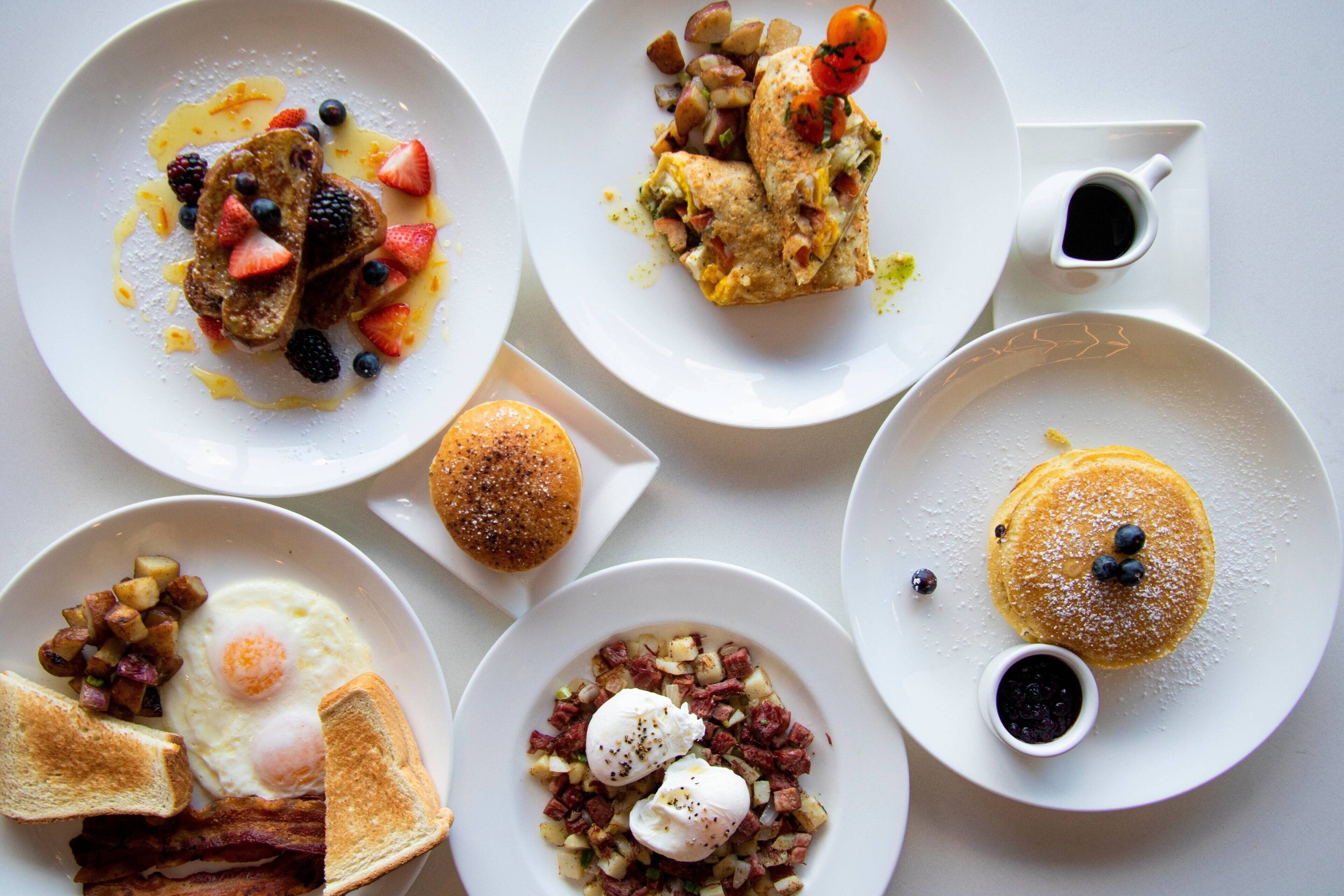 A breakfast spread with pancakes, eggs, toast, and various fruits and condiments.