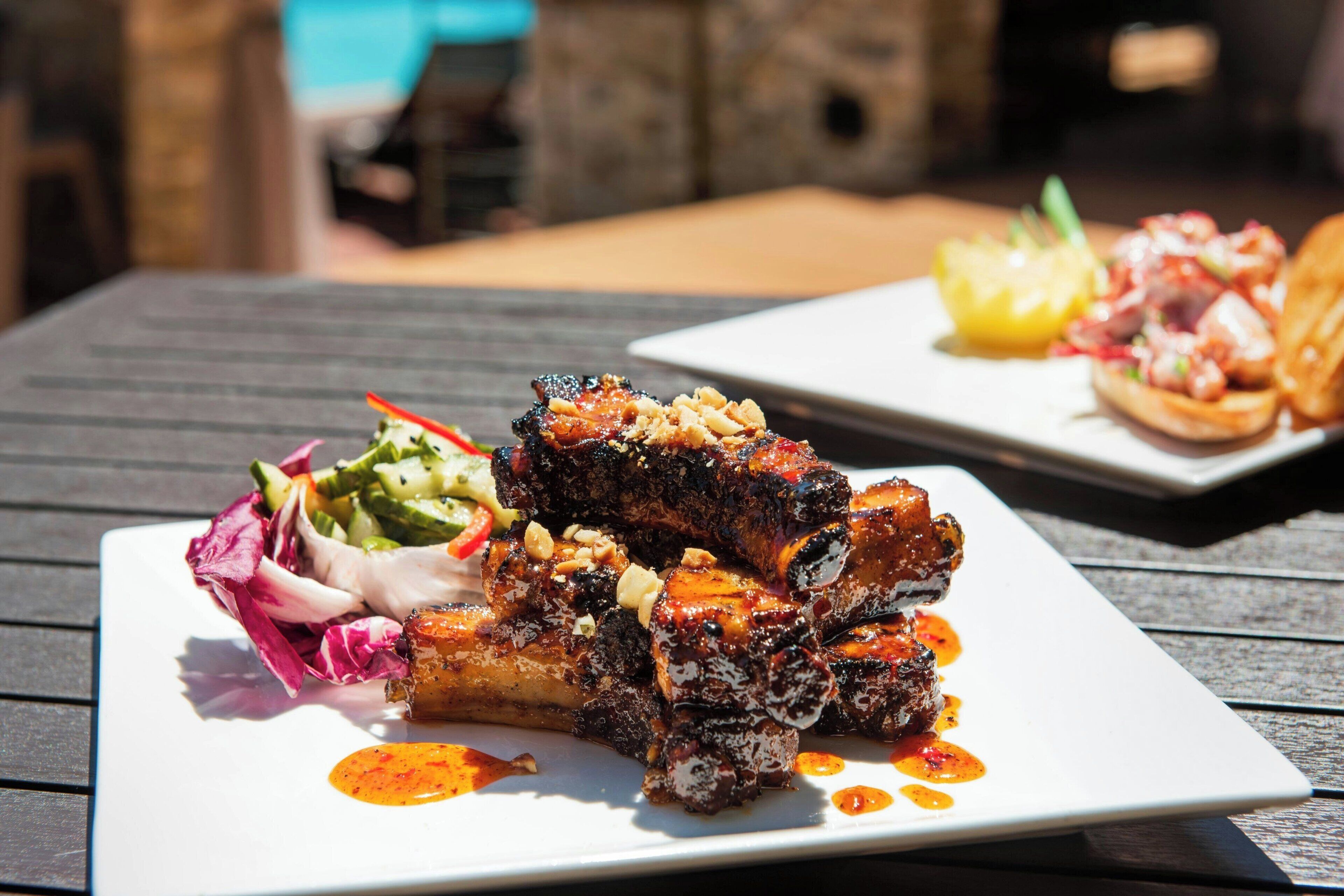 Un plato cuadrado con carne a la parrilla, una ensalada al lado y salsa.