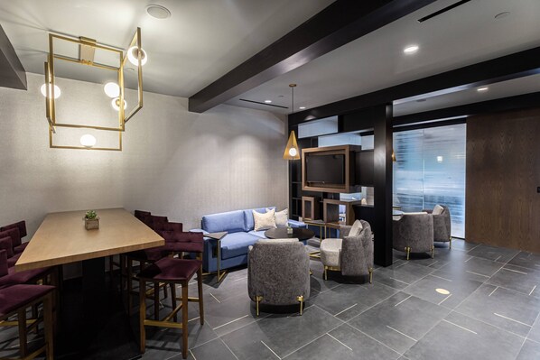A modern lounge area with a wooden table, plush seating, and a television.