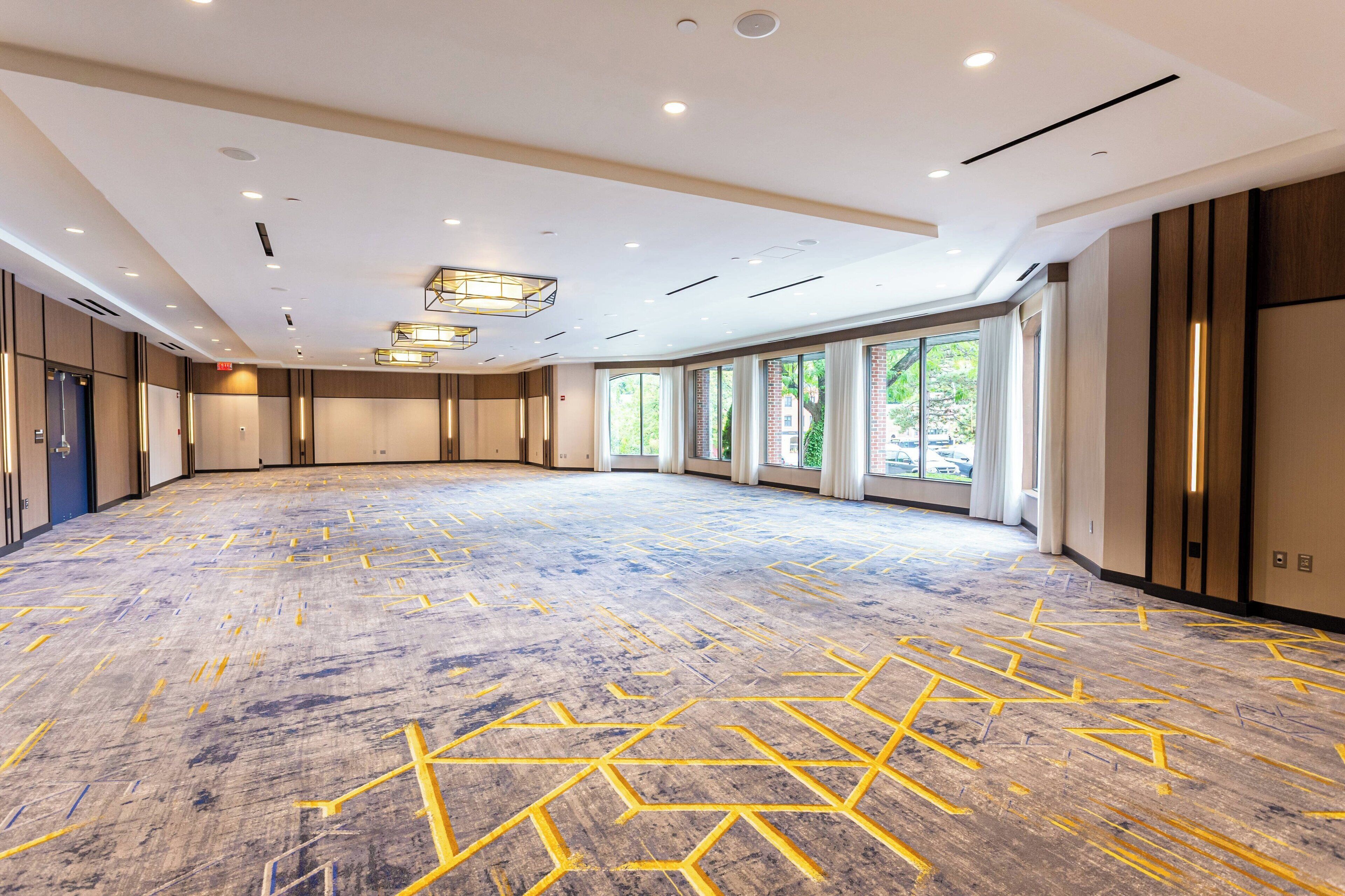A spacious, well-lit conference room with a patterned floor, large windows, and modern lighting fixtures.