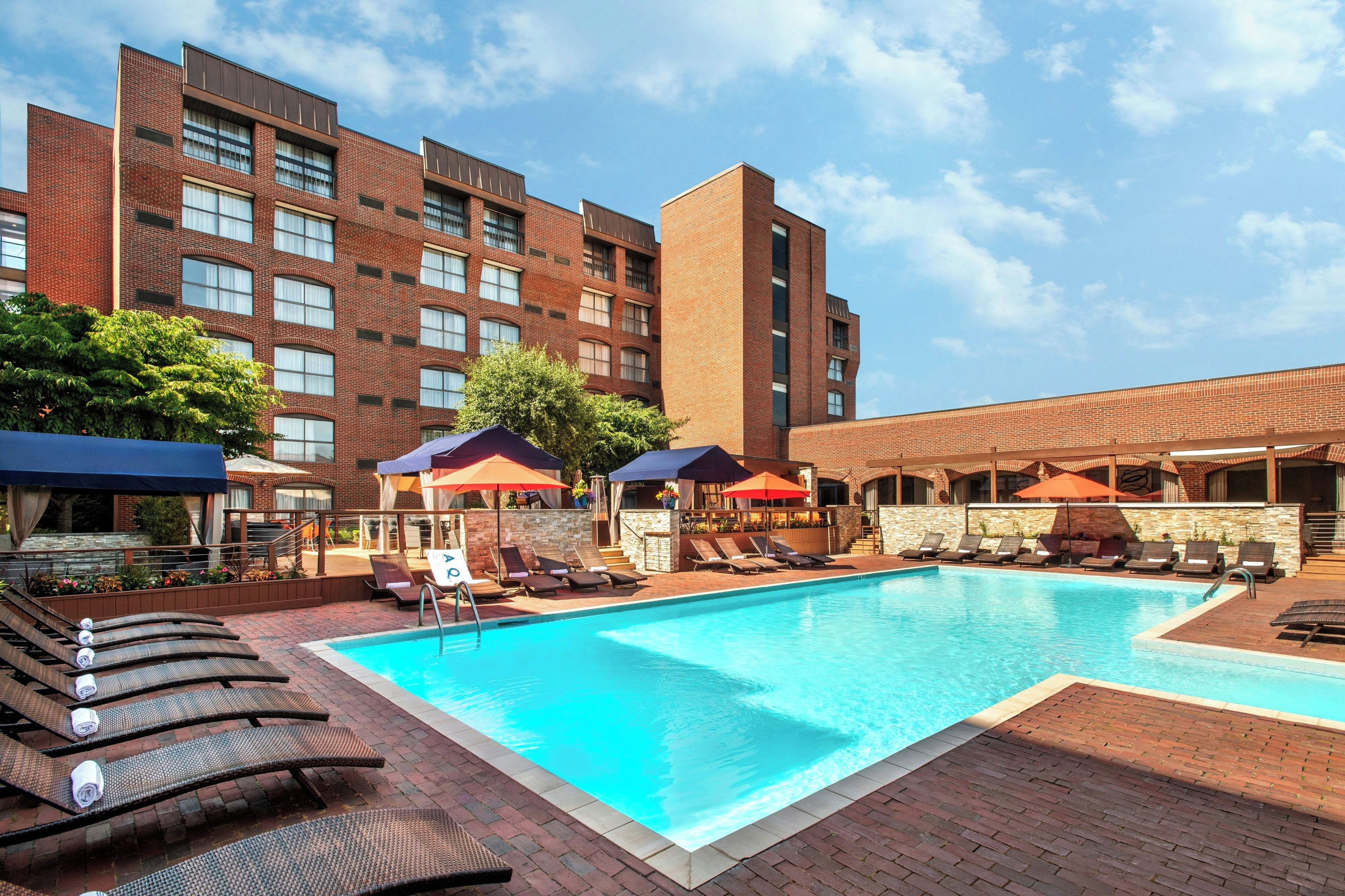 Un espace piscine d’hôtel avec des chaises longues et des parasols, entouré d’immeubles en briques.
