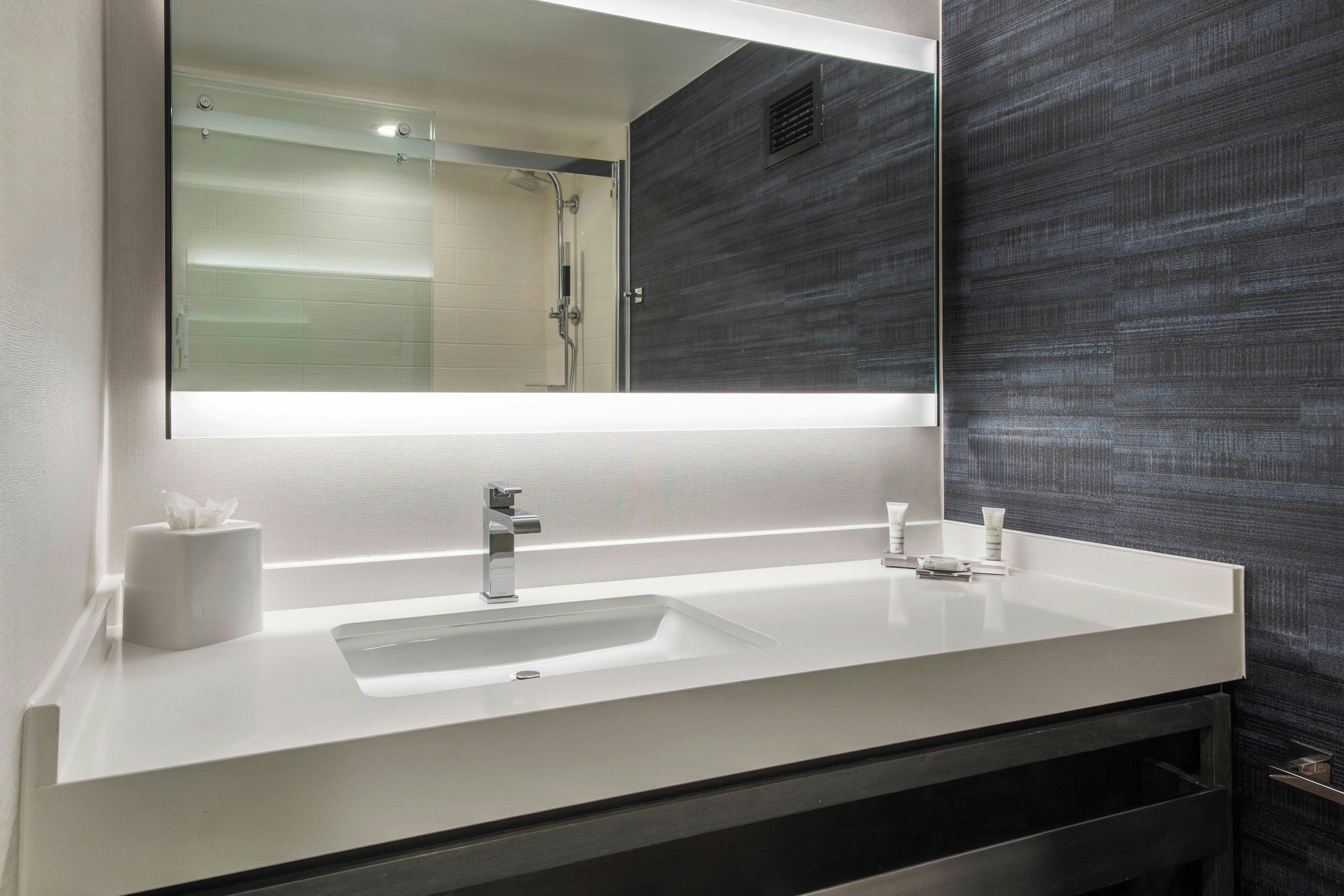 A modern bathroom with a white sink, a large mirror, and a dark textured wall.