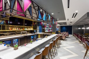 Una zona de bar moderna con una barra larga, taburetes y una variedad de botellas y copas.
