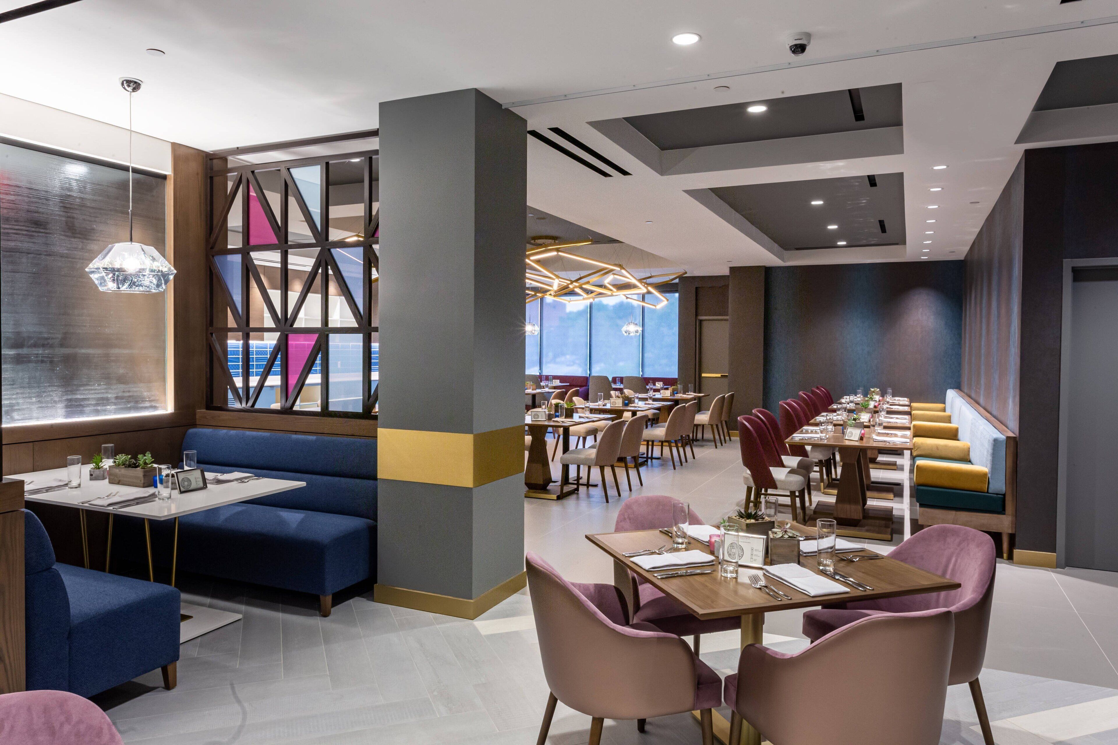 Een modern restaurant met blauwe zitplaatsen, houten tafels en hanglampen.