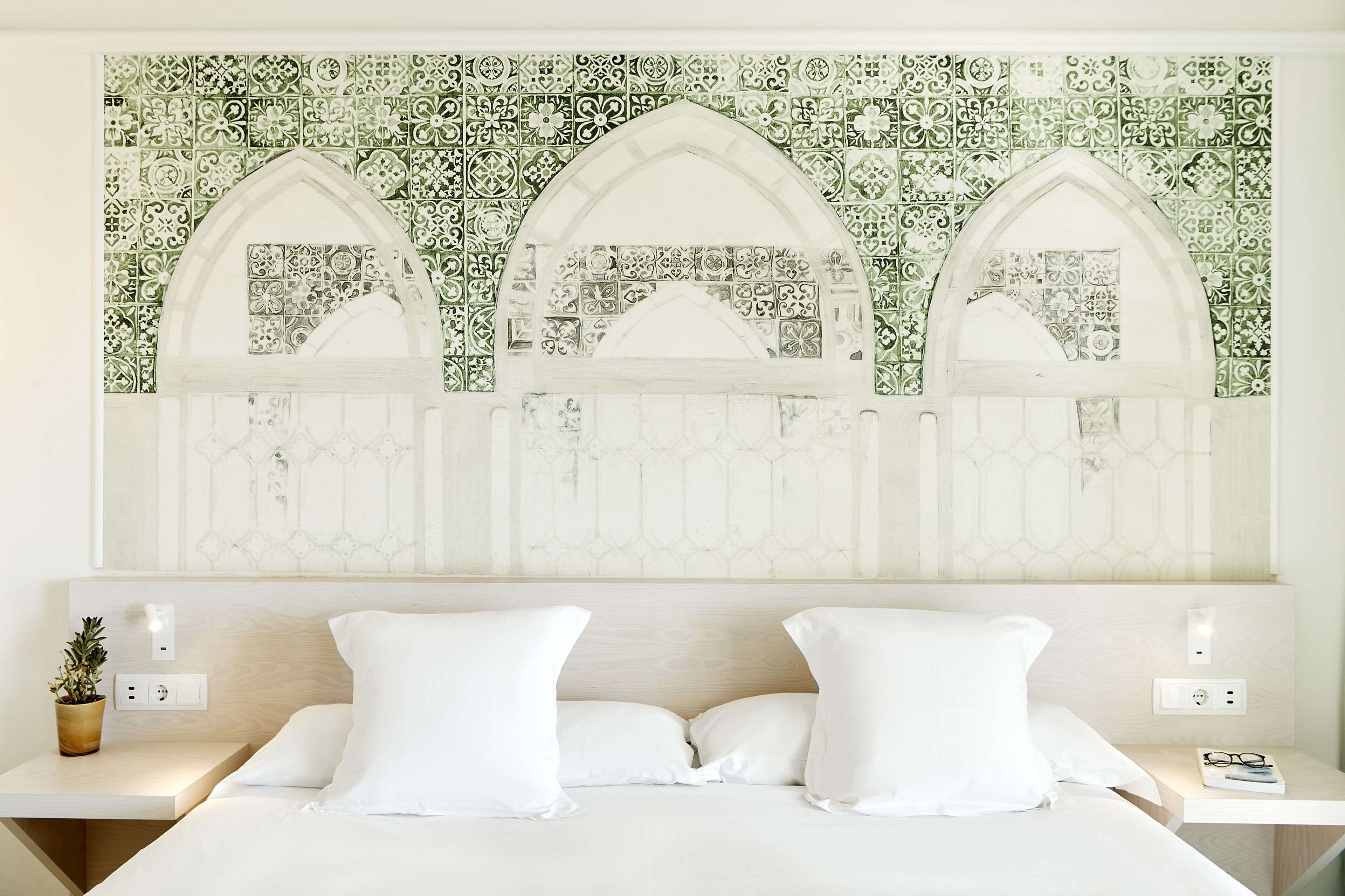 Un dormitorio con cama, dos mesitas de noche y una pared con un diseño decorativo de azulejos.