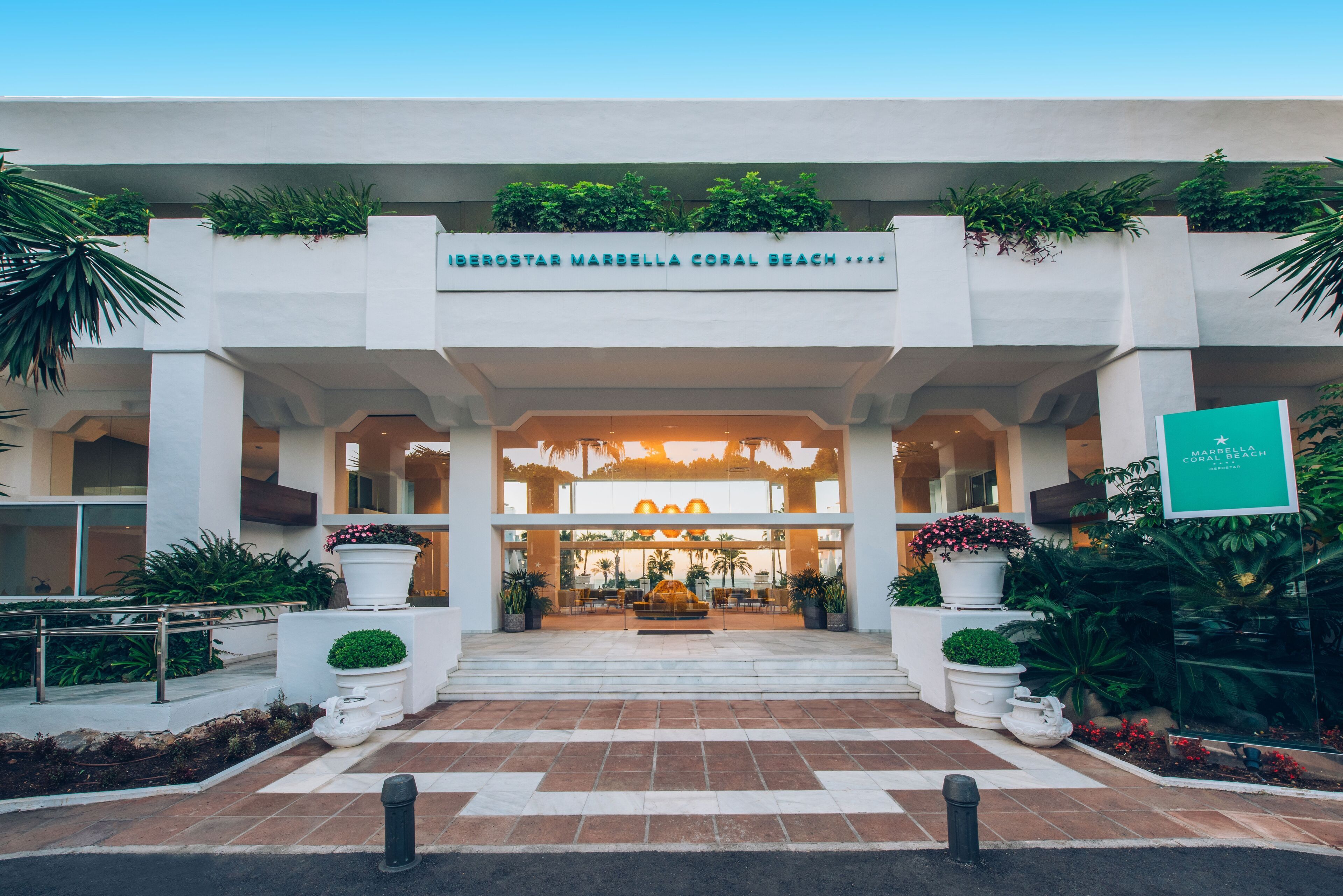 L’entrée de l’hôtel Iberostar Marbella Coral Beach, avec son design moderne, présente une fontaine centrale, des plantes en pot et offre une vue dégagée sur l’intérieur.
