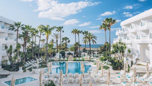 A resort pool area with multiple lounge chairs and umbrellas, surrounded by palm trees and a clear view of the ocean. - Iberostar Selection Marbella Coral Beach (Marbella)