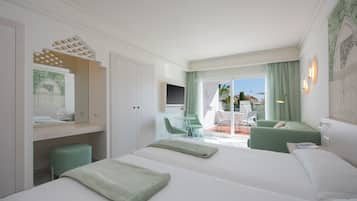 A hotel room with two beds, a TV, a balcony with a table and chairs, and a view of the city.