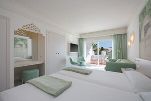 Een hotelkamer met twee bedden, een televisie, een balkon met tafel en stoelen, en uitzicht op de stad.