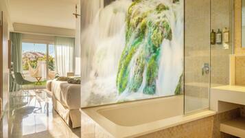 Een moderne badkamer met een groot bad, een douchecabine van glas en uitzicht op een waterval door een groot raam.