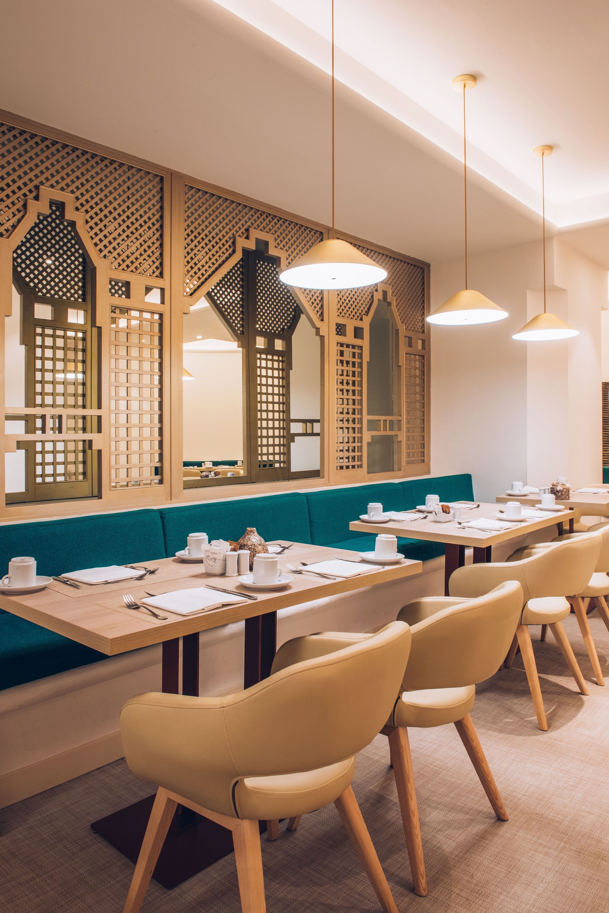 A restaurant with wooden tables, teal cushioned benches, and pendant lighting.