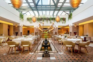 A spacious dining area with a central fountain, surrounded by tables and chairs, under a glass ceiling with hanging plants. - Iberostar Selection Marbella Coral Beach (Marbella)