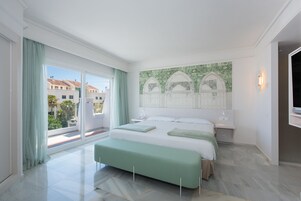 Een moderne slaapkamer met een groot bed, een bankje, uitzicht op gebouwen door een schuifdeur en een decoratief wandpaneel.