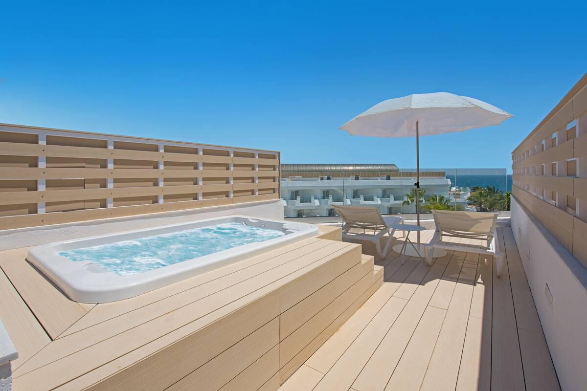Une terrasse sur le toit équipée d’un jacuzzi, de chaises longues et d’un parasol.