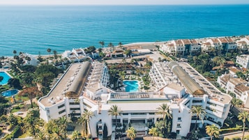 Een resort met meerdere gebouwen, een zwembad in het midden en uitzicht op het strand.