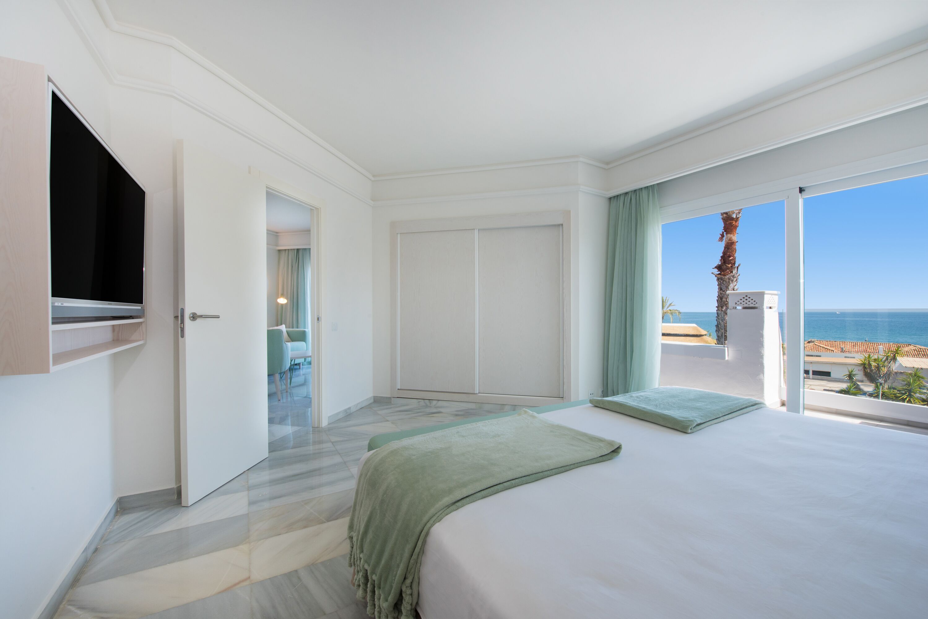 Een hotelkamer met een bed, een televisie, een kast en uitzicht op zee.