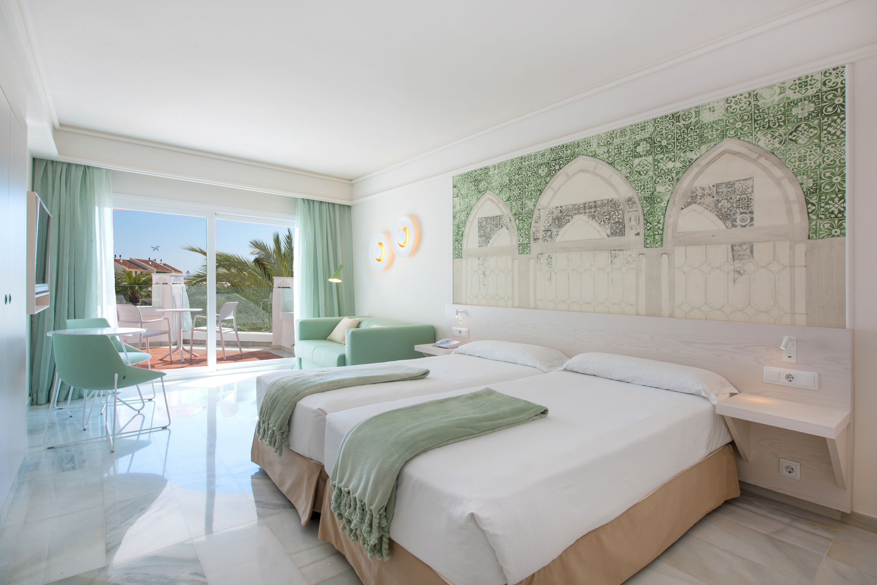 A hotel room with a large bed, a balcony with a view, and a dining area with chairs.