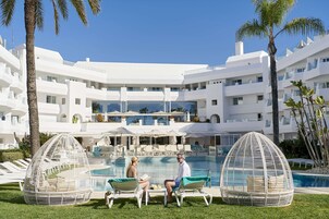 Et resort med swimmingpool, liggestole og en hvid bygning med altaner.