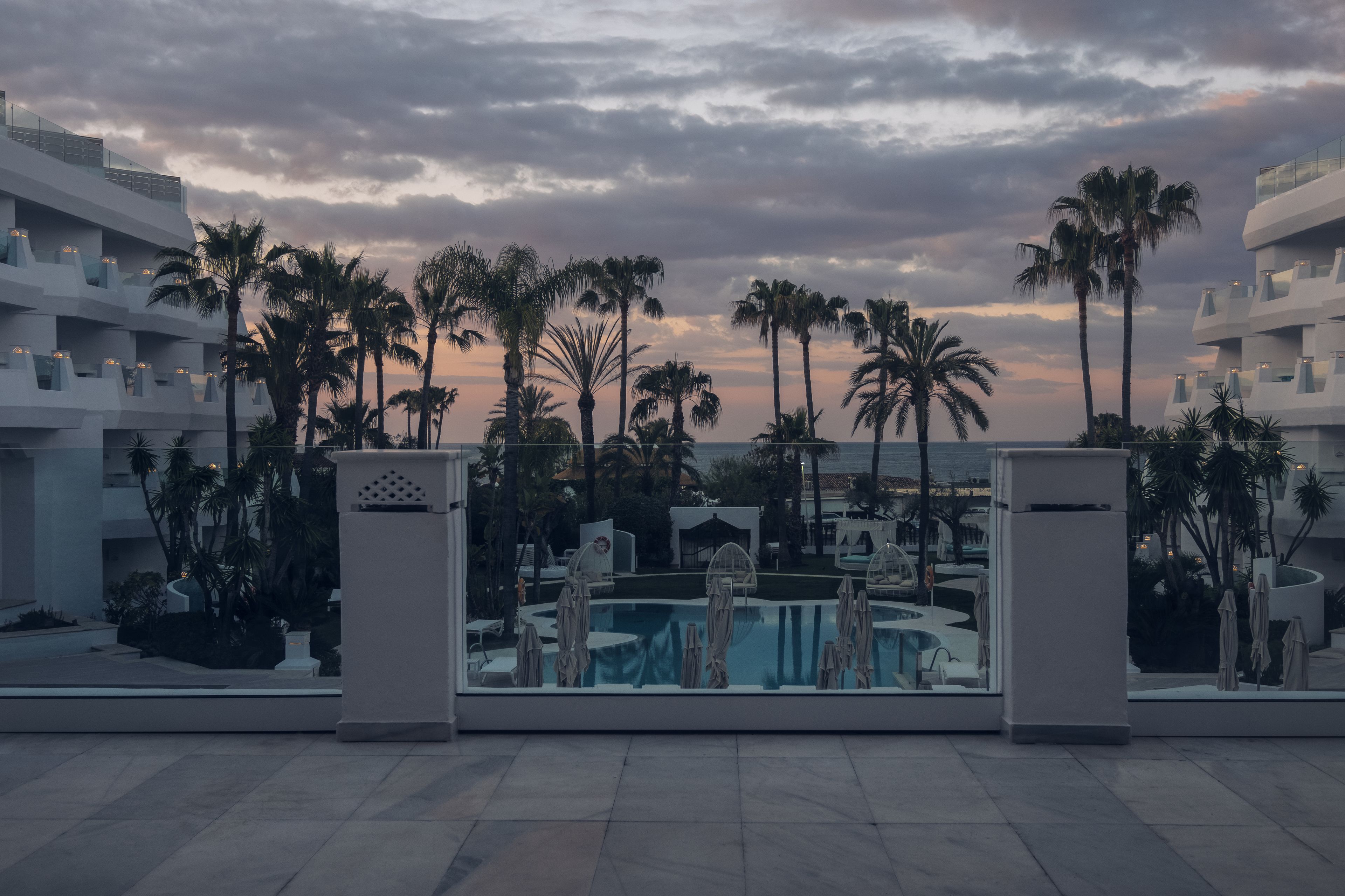 Een modern hotel met een zwembad, palmbomen en uitzicht op de zonsondergang.