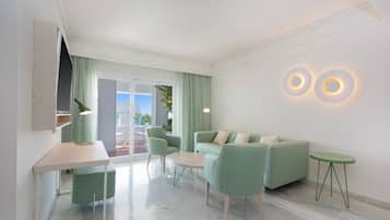 A modern living room with a green sofa, a small table, and a green chair. There is a window with curtains, a lamp, and two wall-mounted lights.
