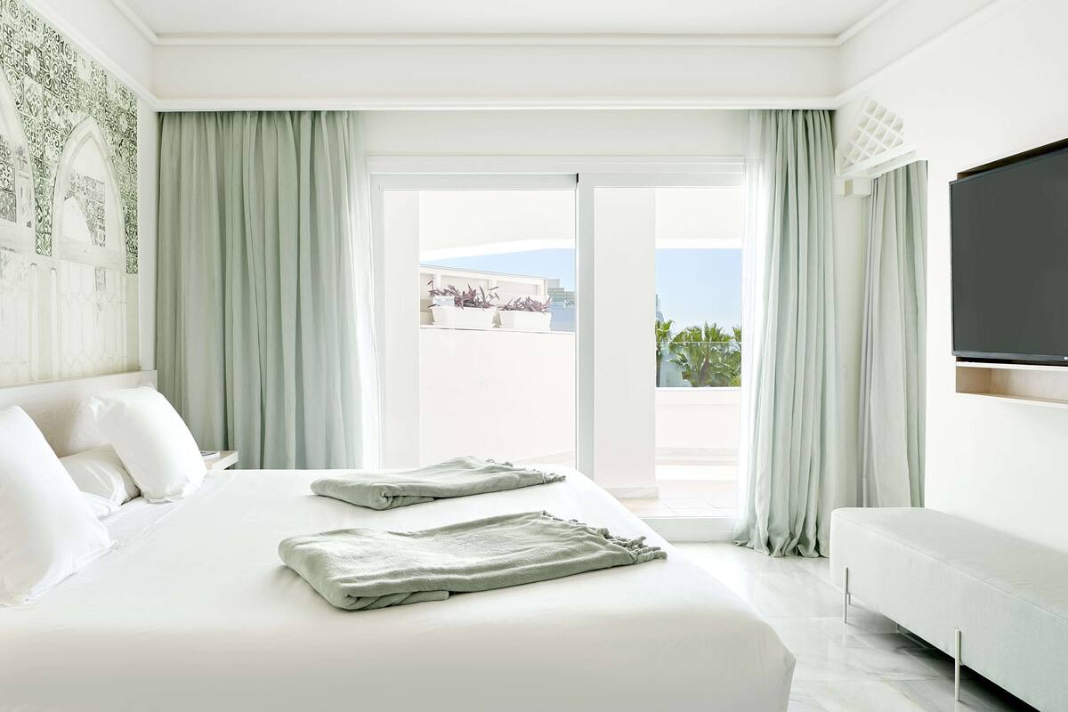 Une chambre d’hôtel avec un grand lit, une télévision à écran plat et un balcon offrant une vue sur la ville.