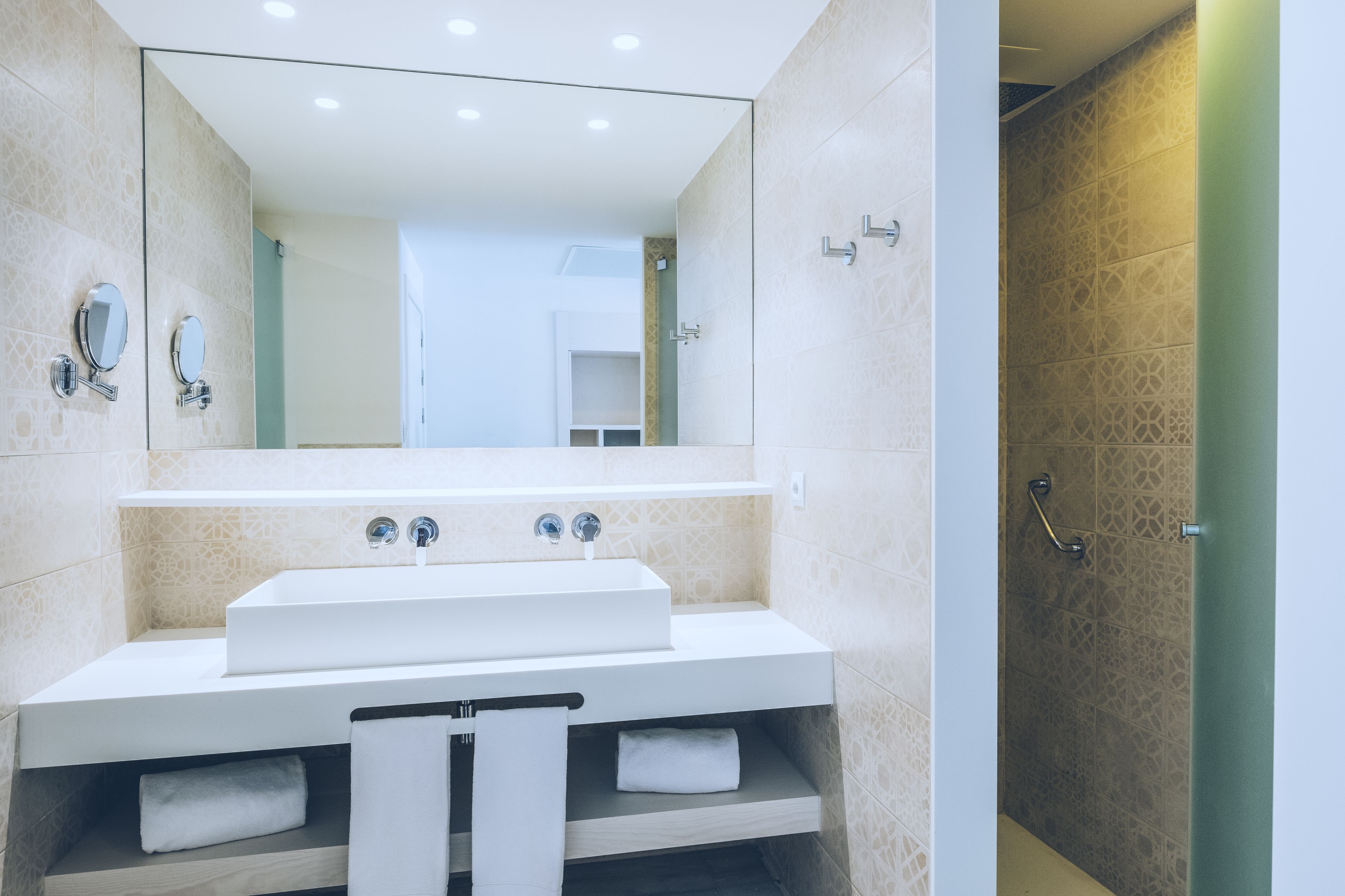 A modern bathroom with a large mirror, a white sink, and a shower area.