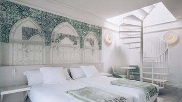 A modern hotel room with a large bed, a skylight, a spiral staircase, and a green chair.