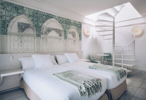 A modern hotel room with a large bed, a skylight, a spiral staircase, and a green chair.