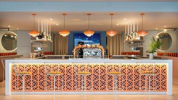 Zona de bar con un separador decorativo, taburetes y luminarias colgantes.