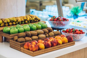 Eine Auswahl an Früchten, darunter Bananen, Äpfel, Kiwis und Pfirsiche, präsentiert auf einem Holztisch.
