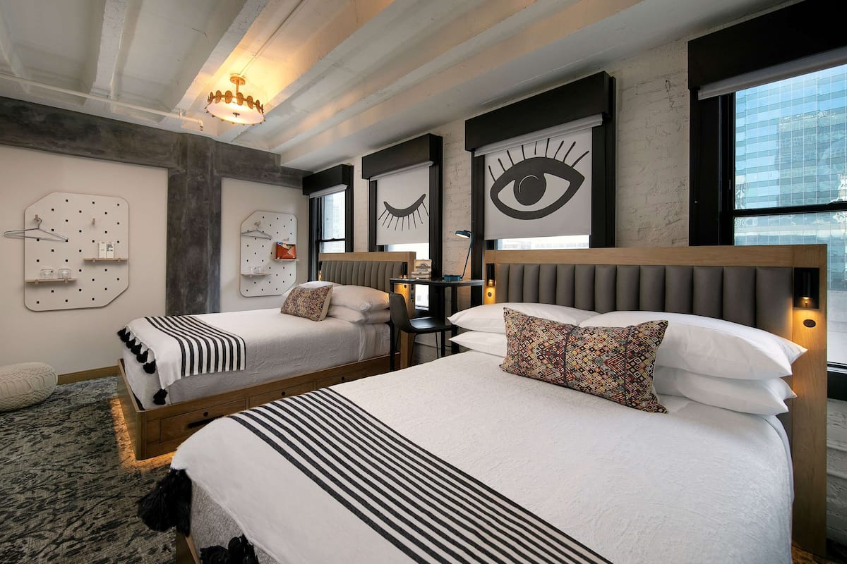 A modern hotel room with two beds, a desk, and a large window.