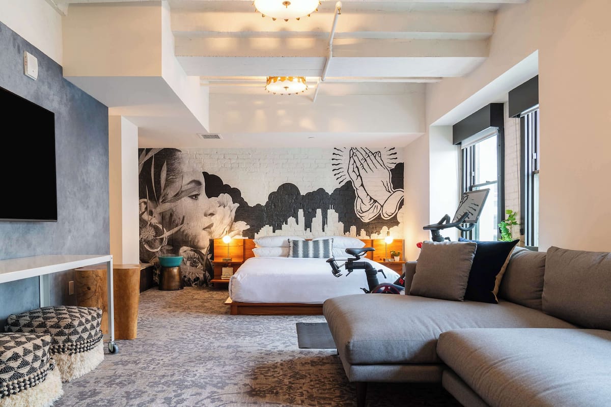 A modern bedroom with a bed, sofa, and a mural on the wall.