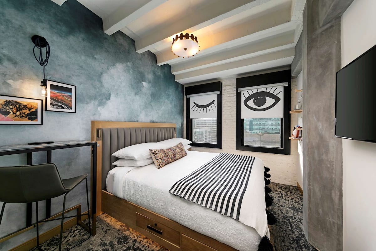 A modern bedroom with a bed, desk, chair, and artwork on the walls.