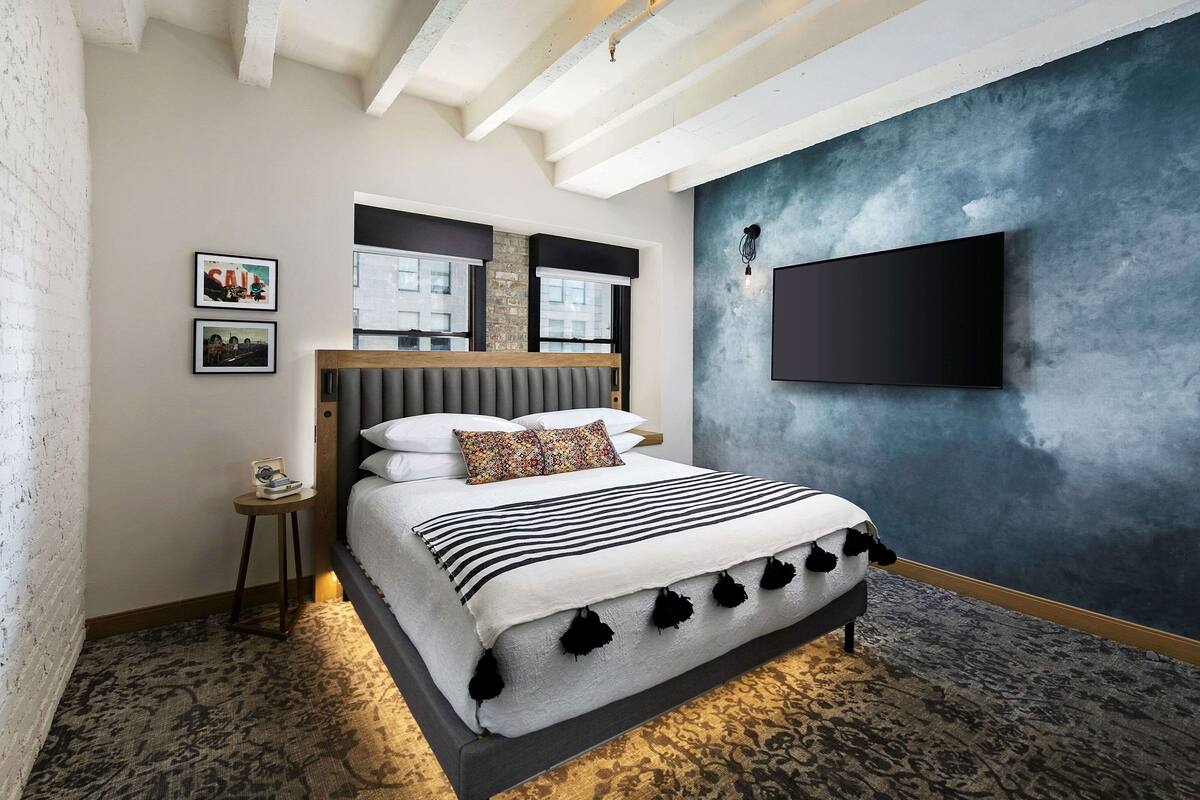 A modern bedroom with a large bed, a TV mounted on the wall, and a small side table.