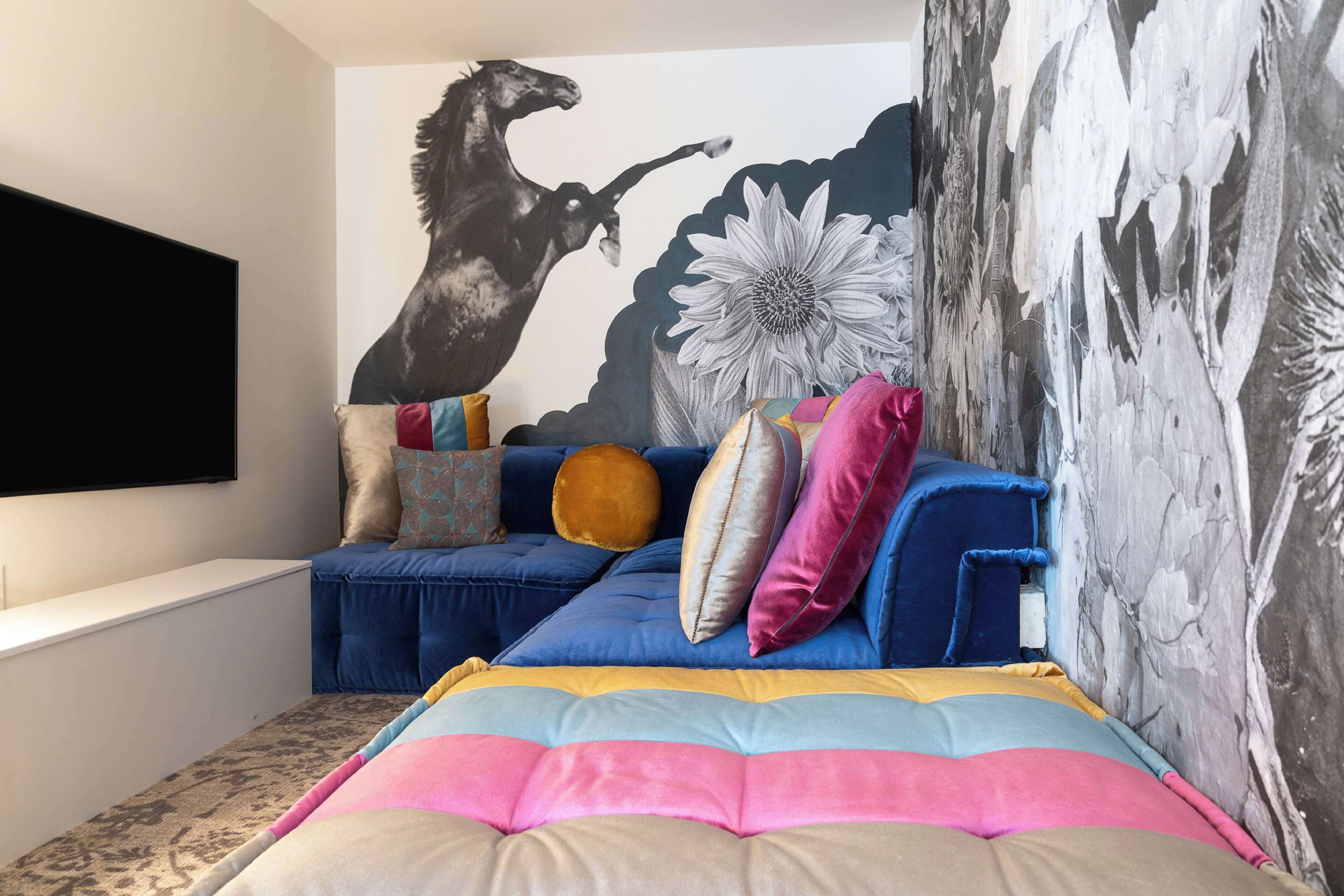 Ein Schlafzimmer mit einem blauen Sofa, bunten Kissen, einem großen Bett und einem Wandbild.