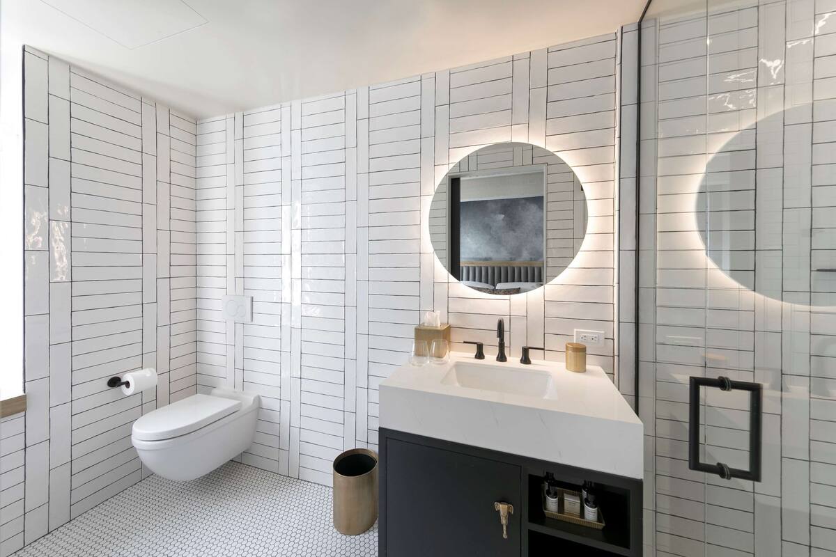A modern bathroom with white tiled walls, a toilet, a sink with a mirror, and a cabinet labeled "Makeup".