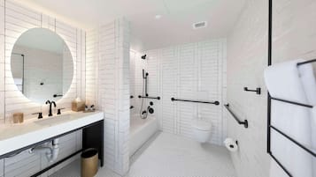 A modern bathroom with a white sink, mirror, and toilet, featuring a hexagonal tile floor and a shower area.