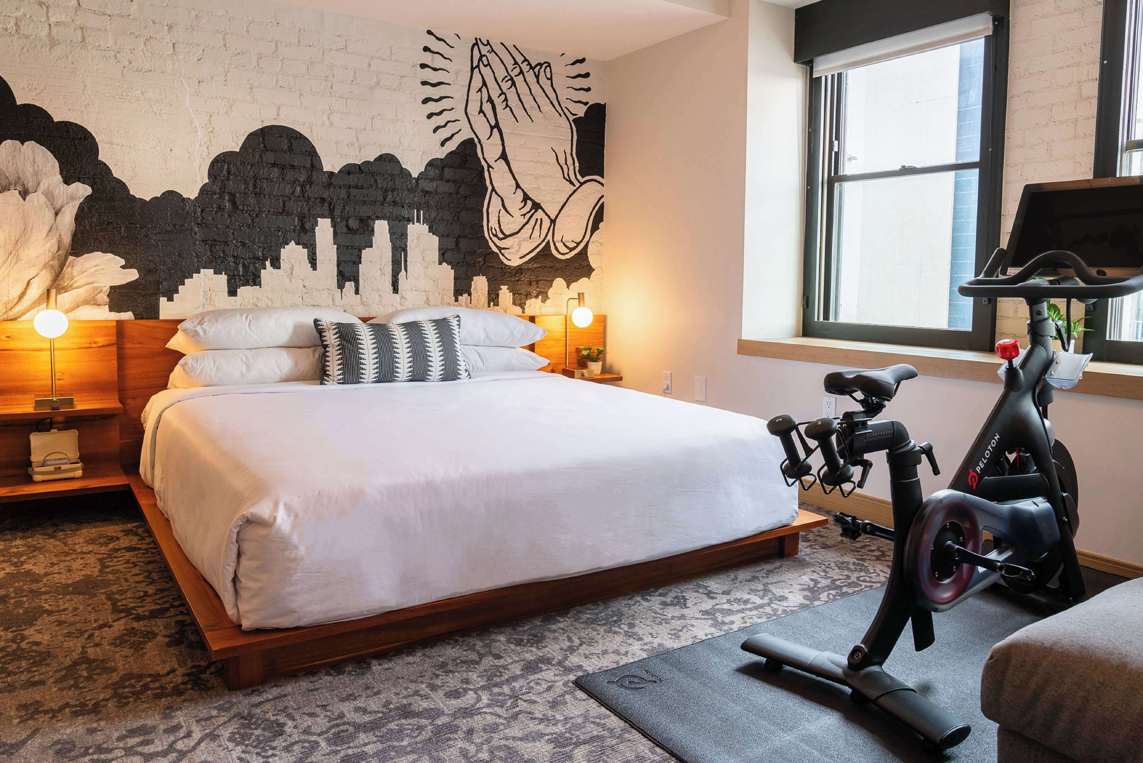 Een slaapkamer met een bed, een muurschildering, een raam en een hometrainer.