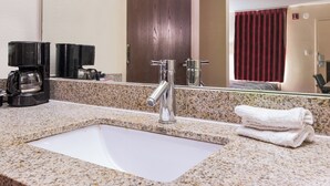 A bathroom with a granite countertop, a sink, a mirror, a towel, and a coffee maker. - Red Roof Inn Texarkana (Texarkana)