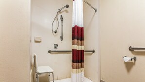 A bathroom with a shower, a toilet, a handrail, and a chair. - Red Roof Inn Texarkana (Texarkana)