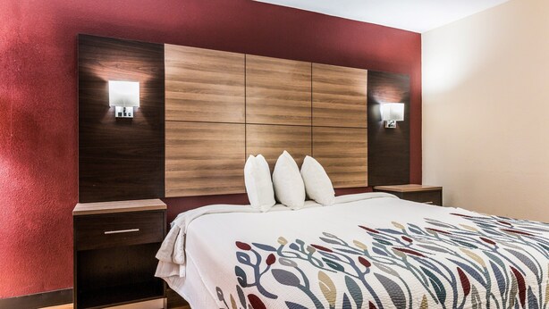 A hotel room with a wooden headboard, two bedside tables, a white bedspread, and two wall-mounted lights. - Red Roof Inn Texarkana (Texarkana)