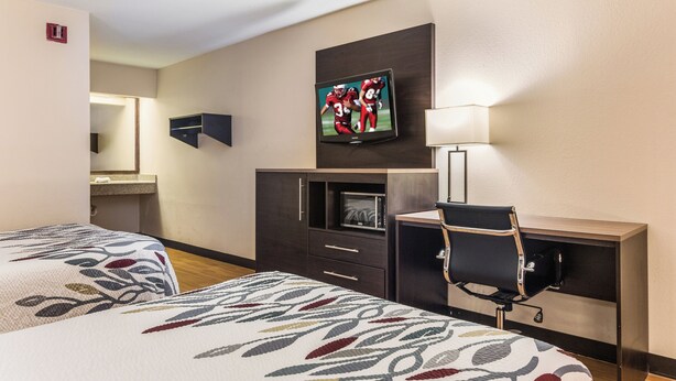 A hotel room with two beds, a desk, a chair, a television, and a microwave. - Red Roof Inn Texarkana (Texarkana)