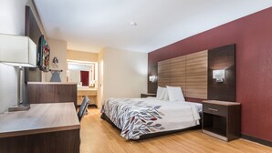 A modern hotel room with a wooden desk, a bed with a patterned bedspread, a nightstand, and a large wall-mounted TV. - Red Roof Inn Texarkana (Texarkana)