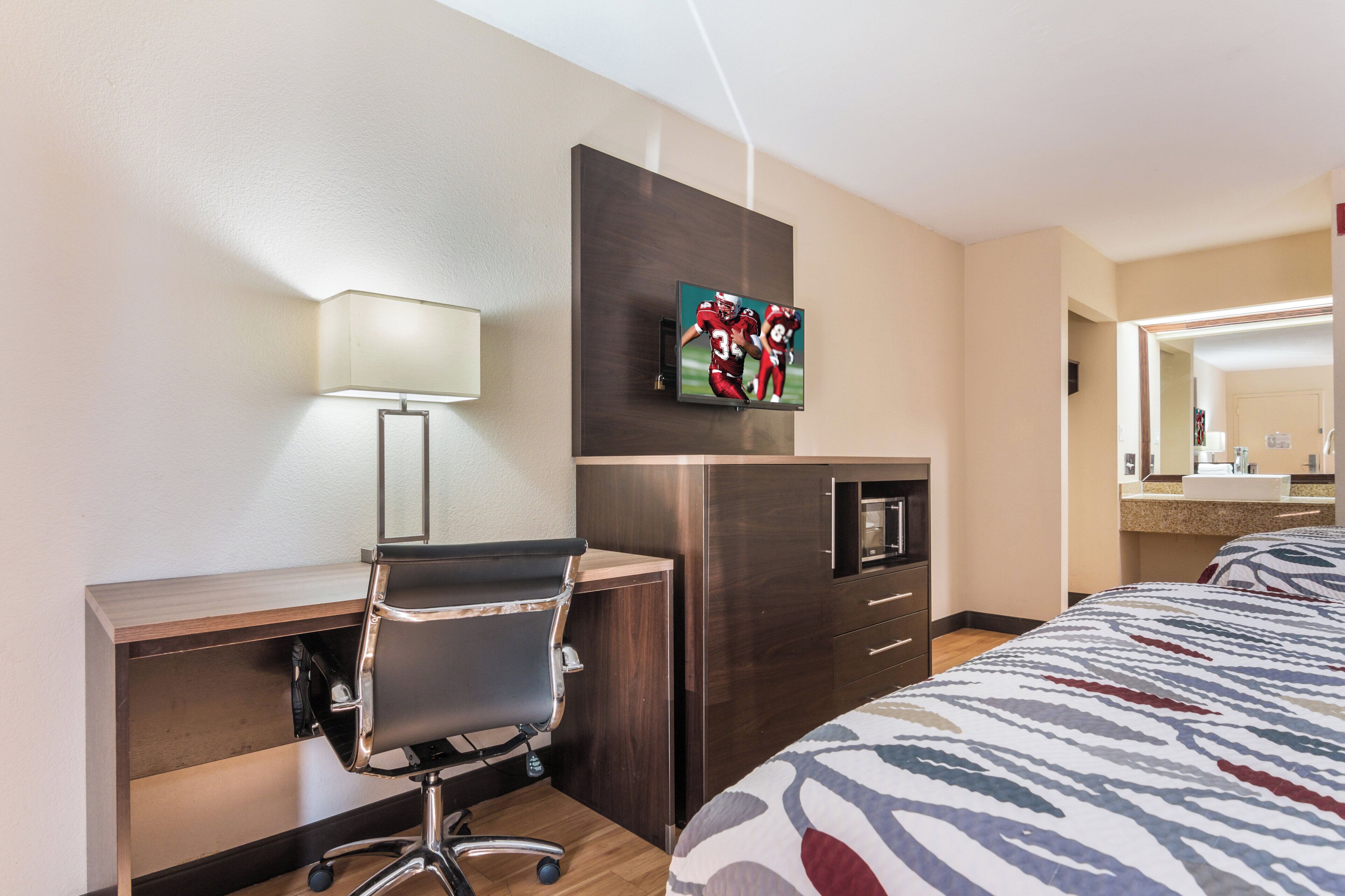 A hotel room with a desk, chair, television, minibar, and a bed.