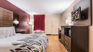 A hotel room with a bed, a TV mounted on the wall, a desk with a lamp, and a wardrobe. - Red Roof Inn Texarkana (Texarkana)