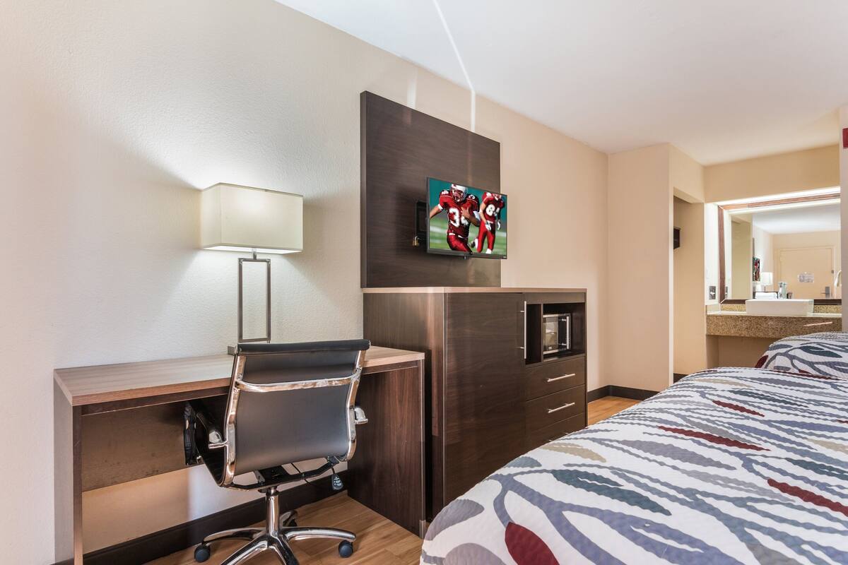 A hotel room with a desk, chair, TV, microwave, and a bed with a patterned bedspread.
