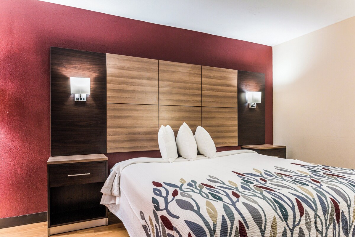 A hotel room with a wooden headboard, bedside lamps, a drawer, and a patterned bedspread.