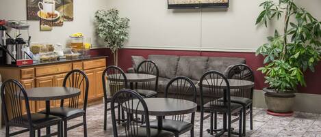 A restaurant interior with round tables and chairs, a bar area with coffee machines, and a television mounted on the wall.